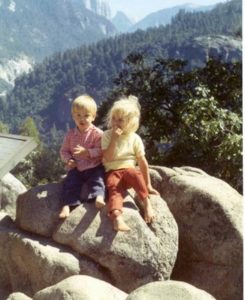 Two small children on a boulder in front of a valley view